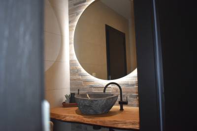 Lavabo avec plan en bois, vasque en pierre et miroir éclairé.